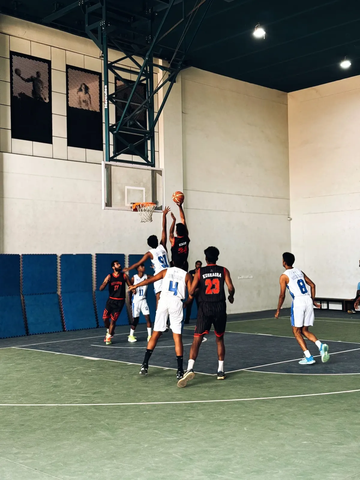 Young players in a game on an indoor basketball court in Bengaluru, one rising to shoot at the hoop.