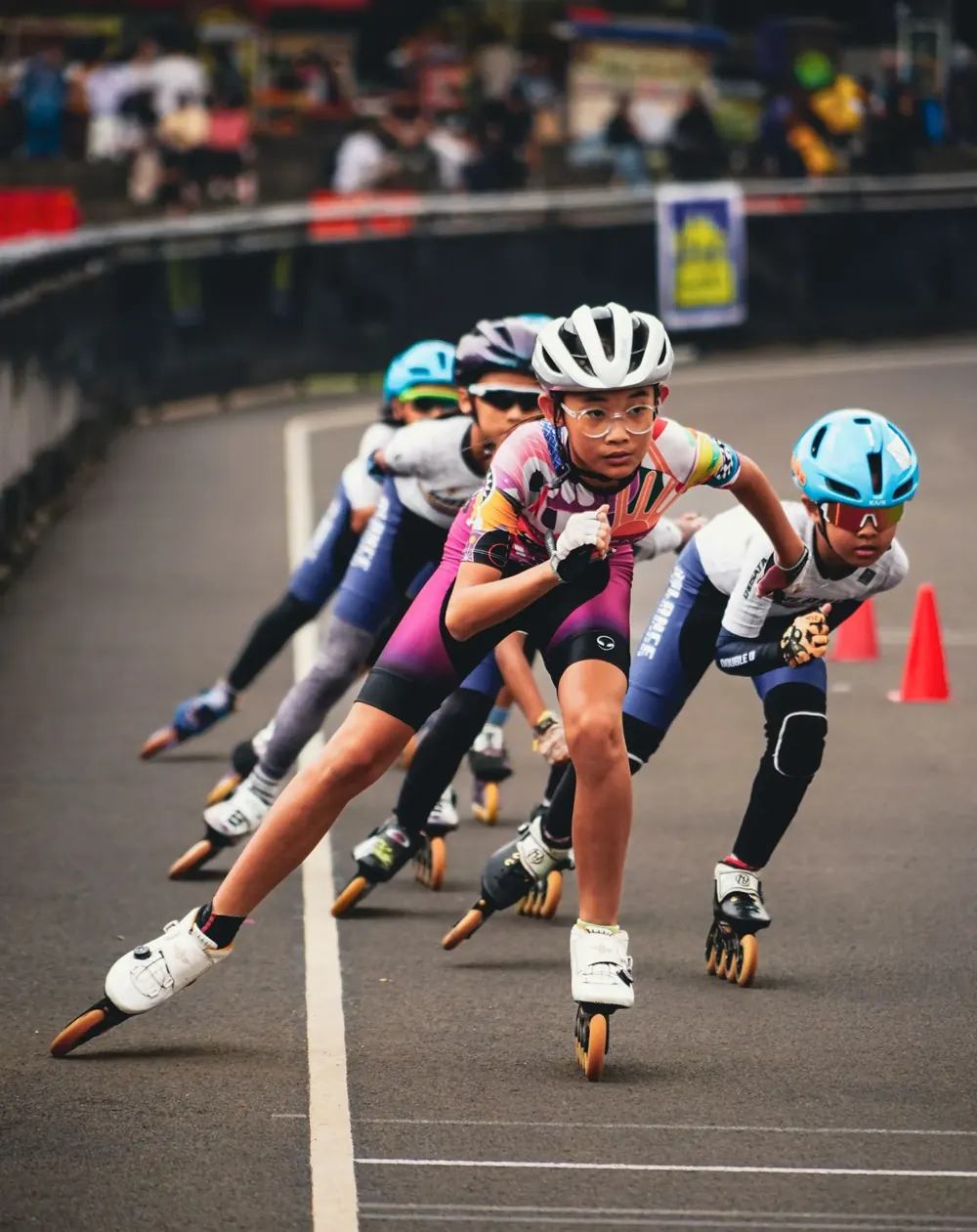 Kids in helmets lean into a bend together during an inline skating race.